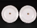 two white plates with gold trims on them on a black surface