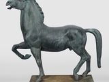 statue d'un cheval au galop posée sur un socle en bois, sur fond blanc