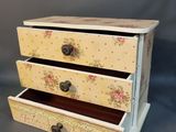 a small wooden box with three drawers on it
