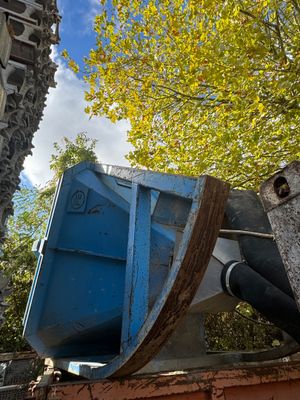 une benne bleue posée contre le mur d'un immeuble, à côté d'un arbre