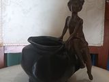 une statue représentant une femme assise sur un vase posé sur une table