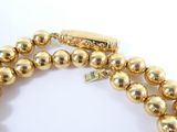 two strands of gold colored beads with a gold clasp on a white background