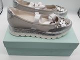 Des chaussures ornées de nœuds sont posées sur une boîte, à côté d'un verre de vin