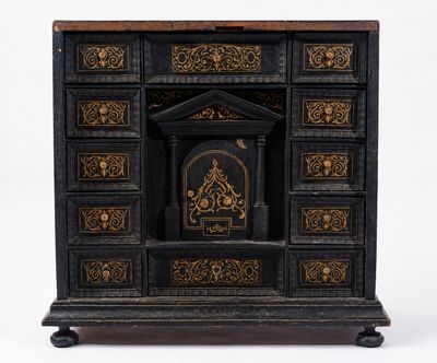 une vieille commode noire et dorée sur laquelle est posée une horloge