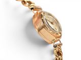a gold watch with a chain around it on a white surface