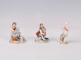 three porcelain figurines of children sitting on a white surface