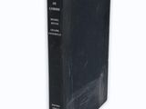 an old book with a black cover sitting on top of a white surface