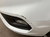 the front of a white car with a dent in it ' s bumper