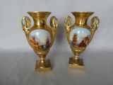 two gold vases with paintings on them sitting on a table