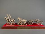 three silver figurines of horses pulling a carriage on a red base