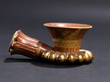 un vase doré muni d'une anse marron, posé sur une surface noire