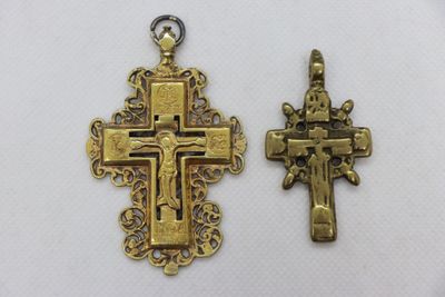 two cross pendants, one gold and one silver, on a white background