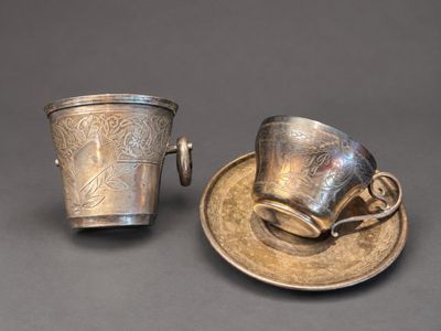 deux tasses et soucoupes en argent posées sur une soucoupe, sur une table