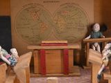 a small doll house with a red roof and two dolls sitting at desks