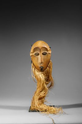 une image représentant un masque en bois aux longs cheveux, posé sur un socle
