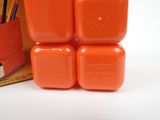 three orange plastic cubes are stacked on top of each other in front of a box of pencils