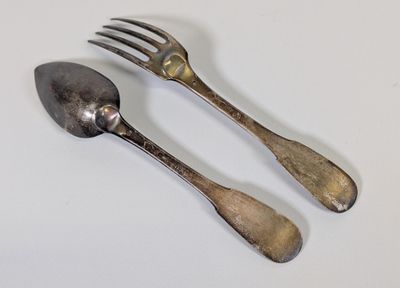 une paire de couverts (une cuillère et une fourchette) posés sur un fond blanc