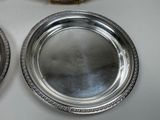 two silver plates on a table with a clock in the background