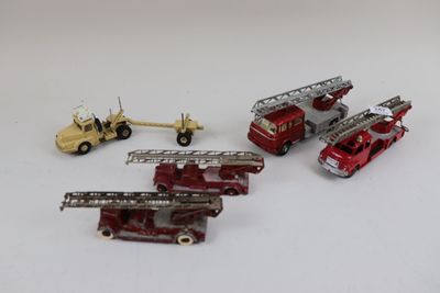 quatre camions de pompiers miniatures et un camion posés sur une surface blanche