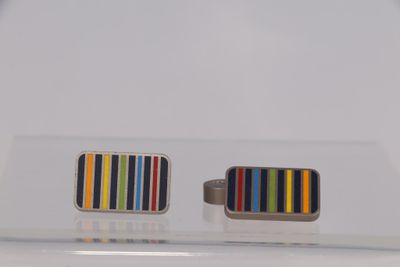 une paire de boutons de manchette ornés de rayures colorées, posés sur une surface transparente