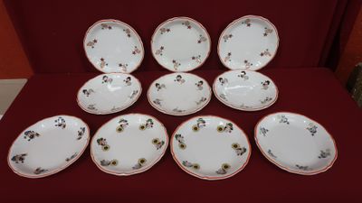 six white and red plates with flowers on them sitting on a red cloth