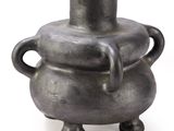 un vase noir avec un couvercle vert posé sur une surface blanche