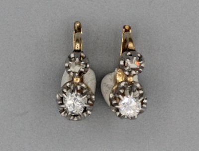 une paire de boucles d'oreilles en diamant et en or posées sur une surface grise