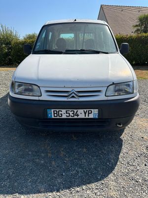 La petite camionnette blanche est garée sur un parking en gravier.