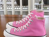 pink converses are on a wooden table with a window in the background