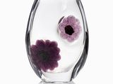 a glass vase with purple flowers in it on a white surface
