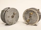 two small metal reels sitting on a white surface
