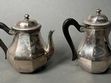 pair of antique silver teapots on grey background with black handles