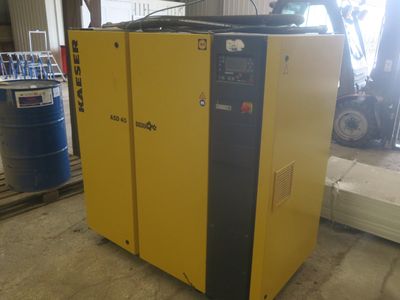 a yellow air compressor sitting in a warehouse next to a blue barrel
