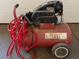 a red air compressor sitting on the floor in a garage