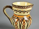 a brown and white pitcher on a stand on a gray surface