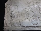a stone relief of a man riding a horse with a cart