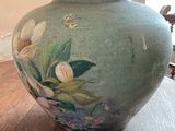 a green vase with flowers painted on it sitting on a table
