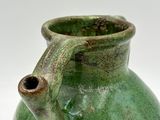 a green vase with a handle sitting on a white surface