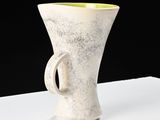 a white vase with a green handle sitting on a table