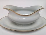 a white and gold gravy dish and saucer on a plate