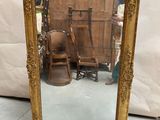 gold framed mirror with a chair and a chair in front of it