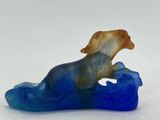 a glass figurine of a dog sitting on a wave