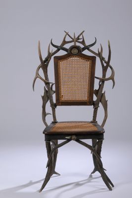 une image représentant une chaise dont le dossier est orné de bois de cerf et dont l'assise est en osier