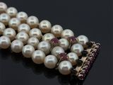 un collier de perles posé sur un fond noir, orné d'une broche rouge et blanche