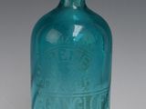 une bouteille en verre bleue avec un bouchon argenté, posée sur une surface blanche