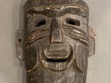 un masque en bois accroché au mur, sur lequel se dessine un sourire