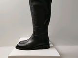 des bottes en cuir noir posées sur une boîte blanche, elle-même posée sur une surface blanche