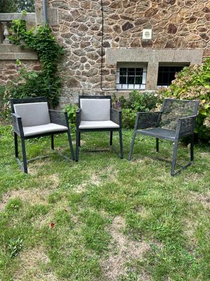 trois chaises et une table posées sur l'herbe, devant un bâtiment en pierre