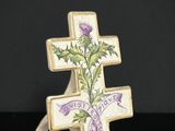 une croix ornée d'un chardon et d'un ruban, posée sur une surface noire