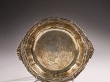 assiette en argent posée sur un support, sur une surface blanche avec un fond gris clair